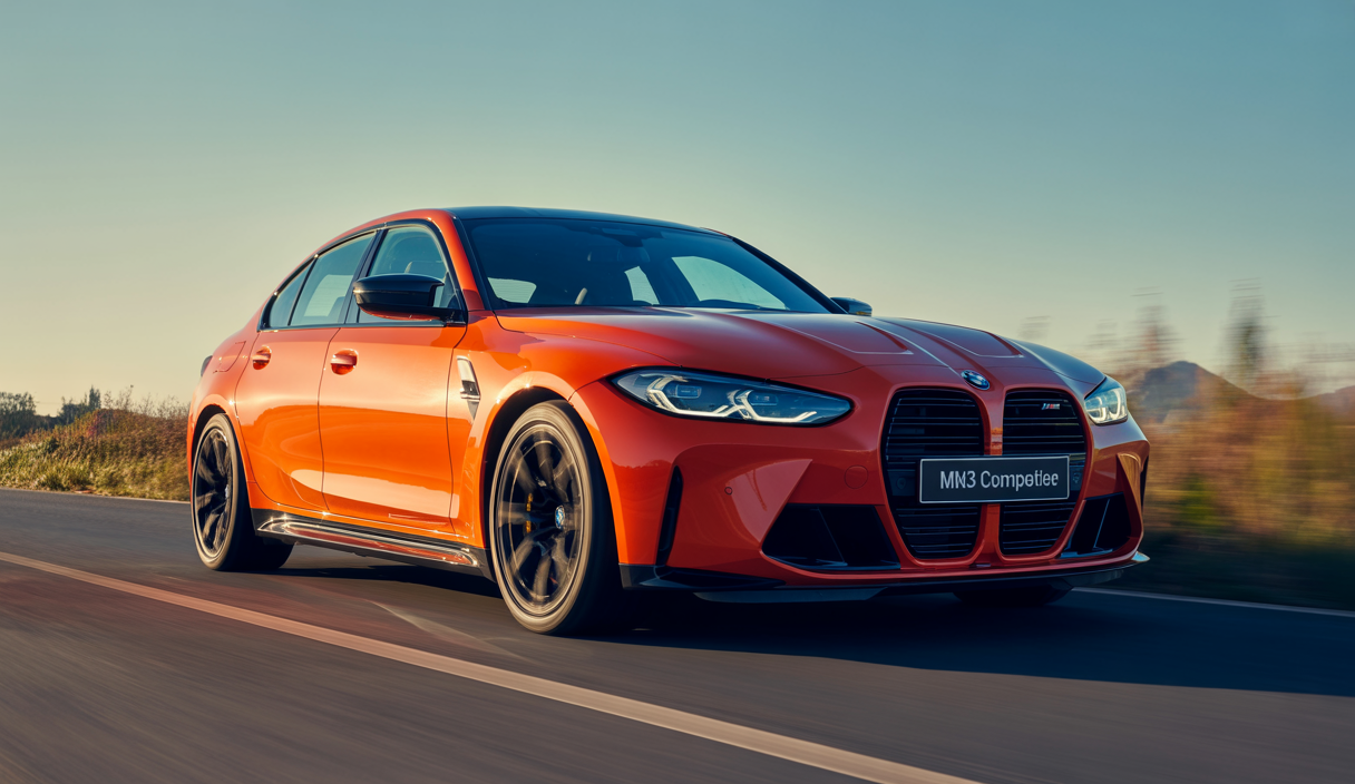 BMW M3 Competition 2025 en teinte Fire Orange vif avec intérieur cuir Merino noir, garée sur une route éclairée par une lumière naturelle douce, soulignant son design sportif et son exclusivité.