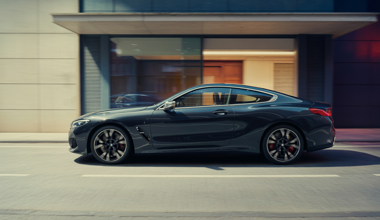 Vue latérale de la BMW 8 Series M850i xDrive noire avec intérieur cuir Merino noir, en ambiance luxueuse et technologique.